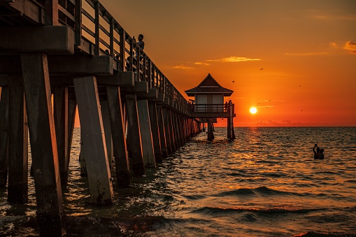 naples, United States – August 10, 2022: A scenic view of people on a wooden pier in the beautiful Naples beach during a mesmerizing sunset
