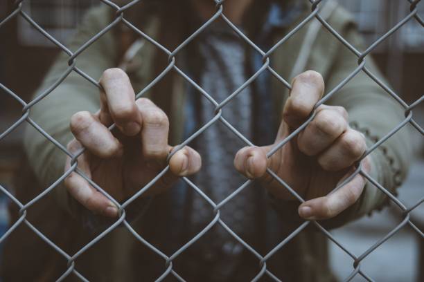 istock Person's hands on a chain linked fence 1440270122