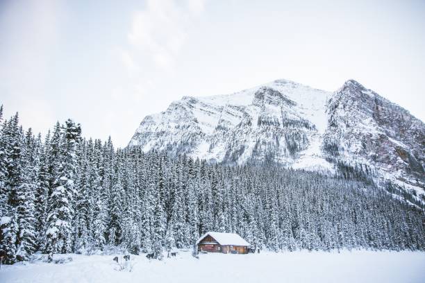 istock A hut in a snowy field with rocky mountains and a forest 1440270141