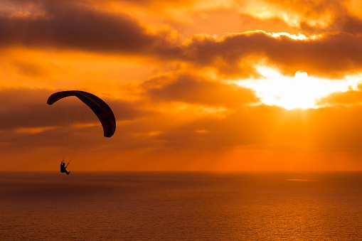 Paragliding at sunset with amazing cloudy sky and the sun shining through clouds