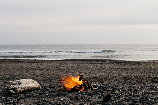 A bonfire at the beach with a cloudy grey sky in the background