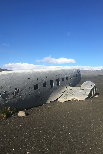 A crashed abandoned airplane in a field with clear blue sky and clouds