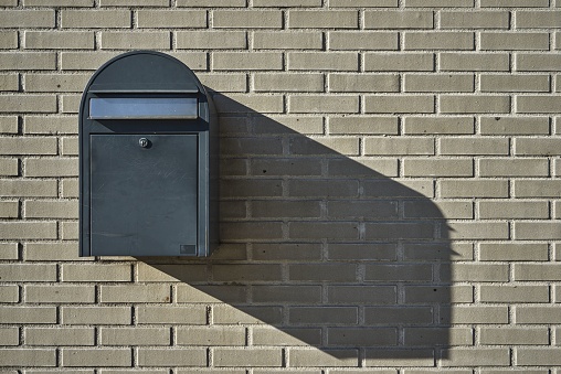 A wall mounted mailbox on a brick wall captured under the sunlight