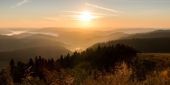 The bright sun in orange sunset sky shining above Black Forest mountain range in Germany