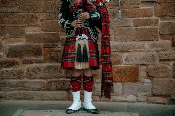 A male wearing traditional Scottish kilt and standing in front of wall
