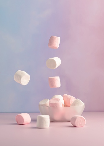 A vertical shot of floating marshmallows over a bowl against a pink and purple background