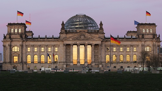 Berlin, Germany – April 10, 2022: The beautiful Bundestag building with the german flags against the sunset sky in Berlin, Germany