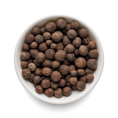 Dry allspice pepper in round bowl isolated on white background. Top view.