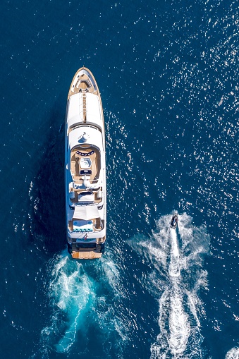 Aerial view of a luxurious white modern expensive yacht moored to a long pier in a bay with crystal clear turquoise ocean water. Close-up. Tourism concept