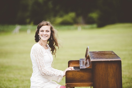 A shallow focus shot of a female playing the piano while smiling at the camera
