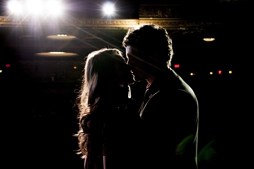 A male and a female kissing each other while standing on the stage in the theatre