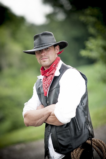 A vertical shot of a cowboy with his hands crossed while looking at the camera