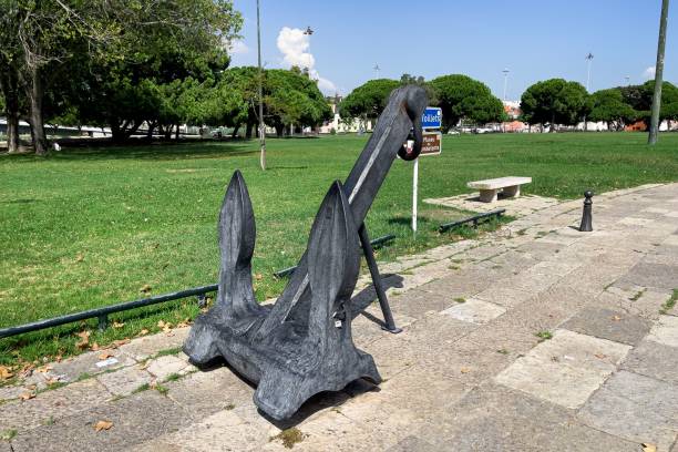 An old ship's anchor on the grass with street lamppost in background.