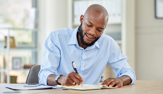 Businessman writing in a notebook while planning a strategy and working in an office. Happy male professional reading and write market search result and work updating schedule at a corporate company