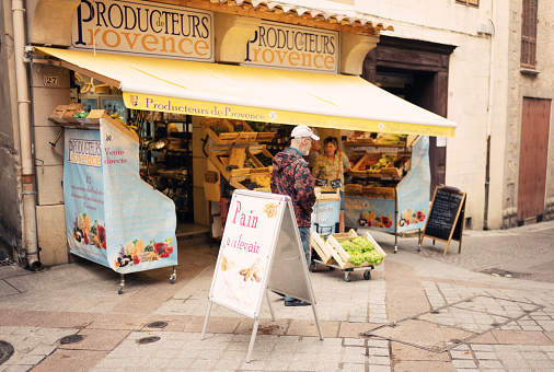 Male local resident walking past a Producteurs de Provence fruit and vegetable shop at 27 Rue Grande in the town of Greoux les Bains in the Provence region of France.