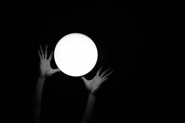 istock Human hands trying to catch an enlightened white circle on black background 1440279234