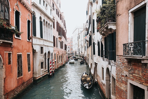 A high angle shot of a beautiful canal in Venice with gondolas  between two buildings