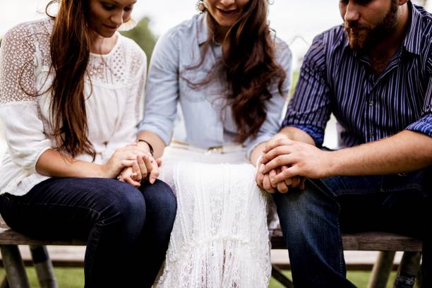 closeup shot of people sitting and holding hands while praying with a blurred background - cross church white heaven imagens e fotografias de stock