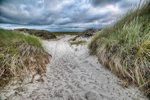 A sandy pathway surrounded by hill under the cloudy sky