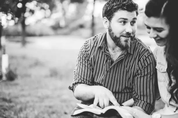 Photo of Grayscale shot of a young Christian couple studying the bible on a blurred background