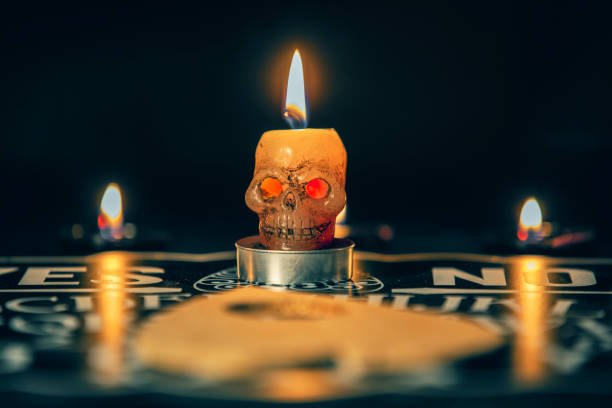 A creepy skull candle with red eyes burning on a spirit board in the dark.