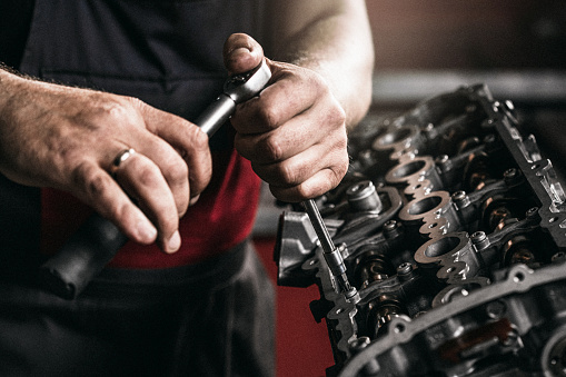 Repairing an engine. Mechanic hands with rotary screwdriver in dark repairshop