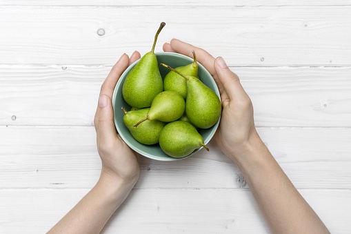 A high angle shot of a person holding a green bowl of pears on a white wooden surface