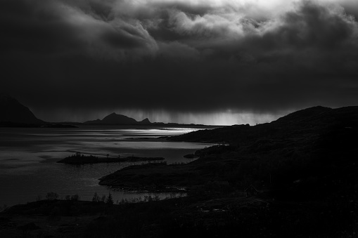 A grayscale shot of silhouettes of hills and a lake under the sky with dark clouds - depression concept