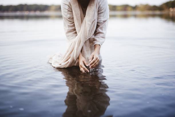 istock Female wearing a biblical robe while standing in the water and washing her hands 1440283381