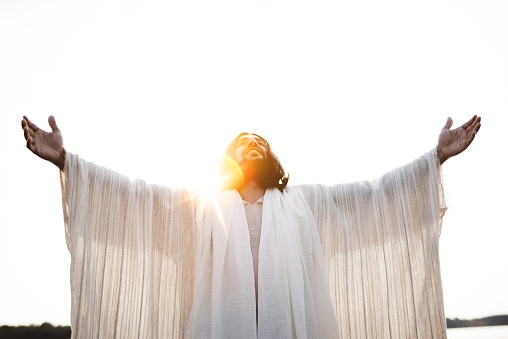 The Jesus Christ with his hands open and towards the sky with the sun shining in the background