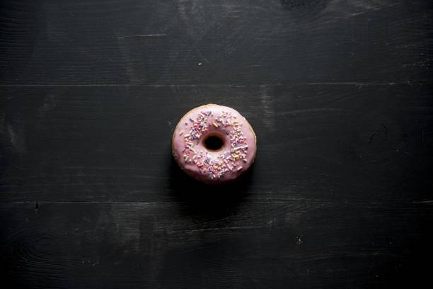 istock Overhead shot of a pink donut with sparkles on a black surface 1440283644