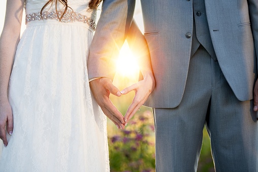A beautiful shot of bride and groom making a heart shape with their hands and the sun shining in the background