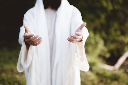 A closeup of Jesus Christ reaching out with a blurred background