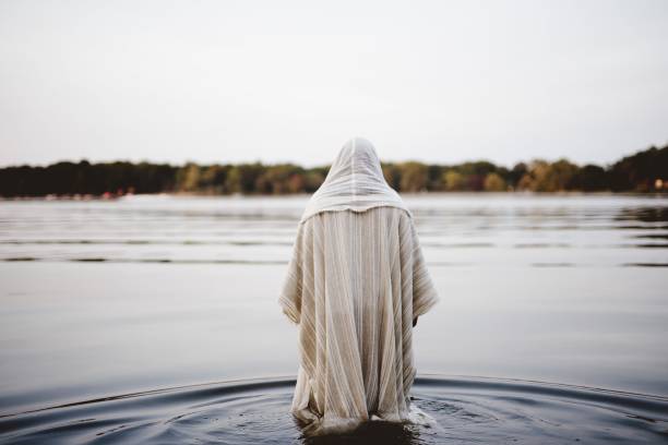 Person wearing a biblical robe walking in the water with a blurred background shot from behind A person wearing a biblical robe walking in the water with a blurred background shot from behind prophet stock pictures, royalty-free photos & images