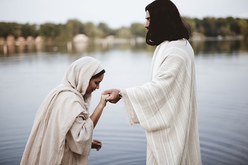 A shallow focus shot of a female wearing a biblical gown while holding the hand of Jesus Christ