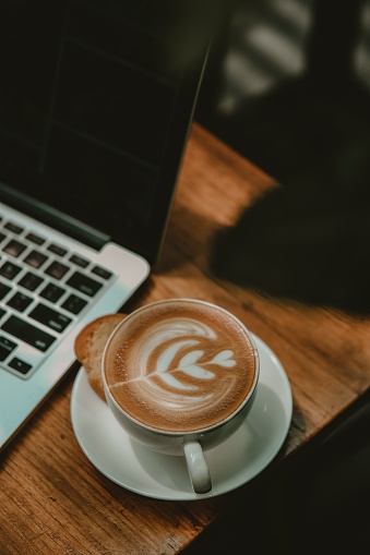 A vertical shot of a cup of latte art next to a laptop