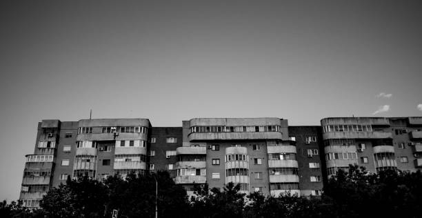 A greyscale low angle shot of an old building with a small park in the front