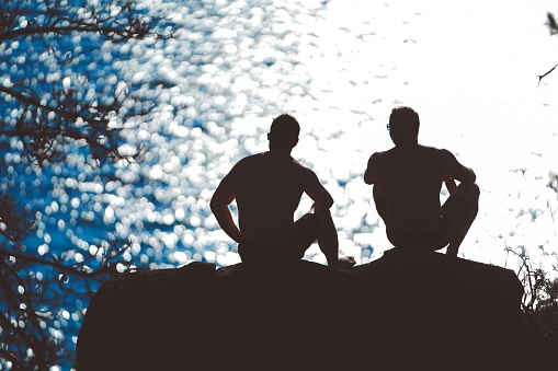A silhouette of two friends sitting on a rock near the sea enjoying each others company in the evening