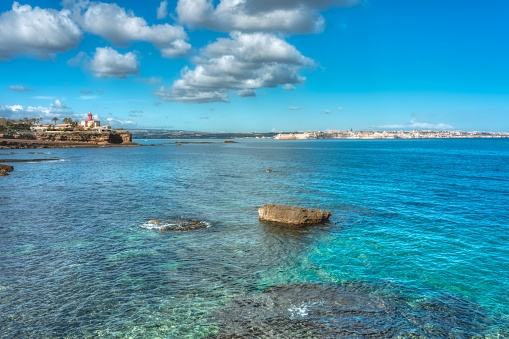 A wide shot of a beautiful calm sea and a coastline with buildings under the cloudy sky