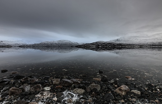 A beautiful shot of rocks on the body of water surrounded by fjord under a gray cloudy sky