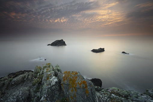 A calm day at the ocean with rocks in the middle and the sky shining lightly in Pentire Point East, Cornwall, UK
