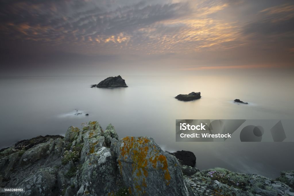 Calm day at the ocean with  the sky shining lightly in Pentire Point East, Cornwall, UK A calm day at the ocean with rocks in the middle and the sky shining lightly in Pentire Point East, Cornwall, UK Atlantic Ocean Stock Photo