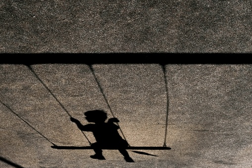 A horizontal shot of the shadow of a child on a swing on a grey wall