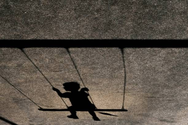 Horizontal shot of the shadow of a child on a swing on a grey wall A horizontal shot of the shadow of a child on a swing on a grey wall religion sunbeam one person children only stock pictures, royalty-free photos & images