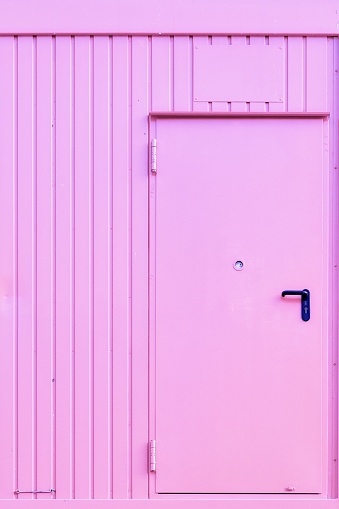 A vertical shot of a pink wall with a pink metallic door and a blue handle. Perfect for a background.