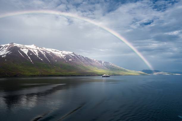l'arcobaleno sul mare vicino alle montagne innevate e una nave isolata - rainbow harbor foto e immagini stock