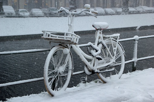A bicycle leaned against a fence near the water covered in snow