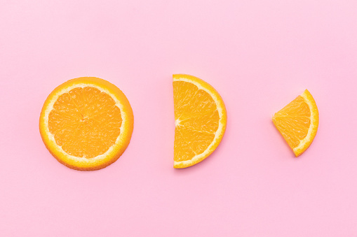 A top view of differently shaped orange slices on pink bakcgeoun