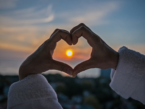 Hands in heart shape at sea and sunset background