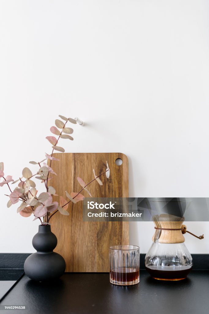 chemex with black filtered coffee and glass on table indoors detail of decor at kitchen, modern vase with eucalyptus branch near caffeine beverage in glass chemex, alternative method of brewing fresh coffee at home Apartment Stock Photo